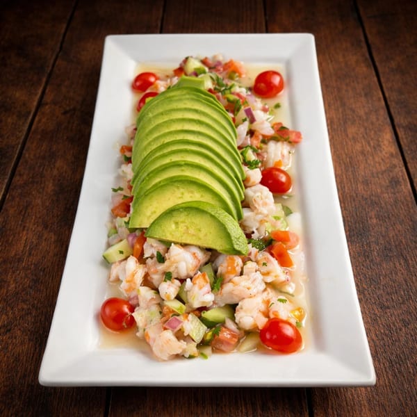 Shrimp ceviche with sliced avocado, cherry tomatoes, and diced vegetables on a white rectangular plate.