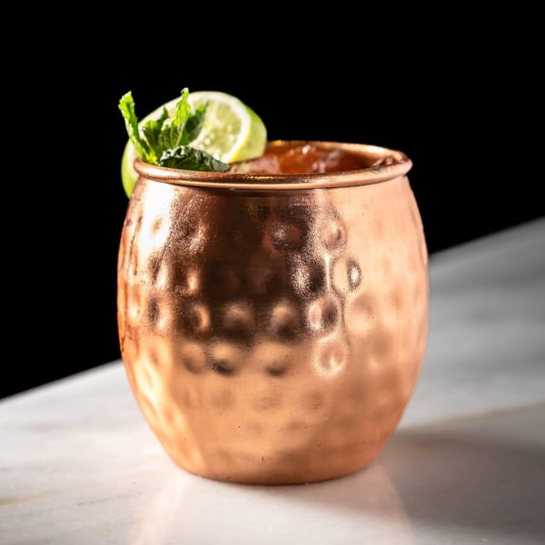 A Moscow Mule cocktail in a hammered copper mug, garnished with lime and mint.